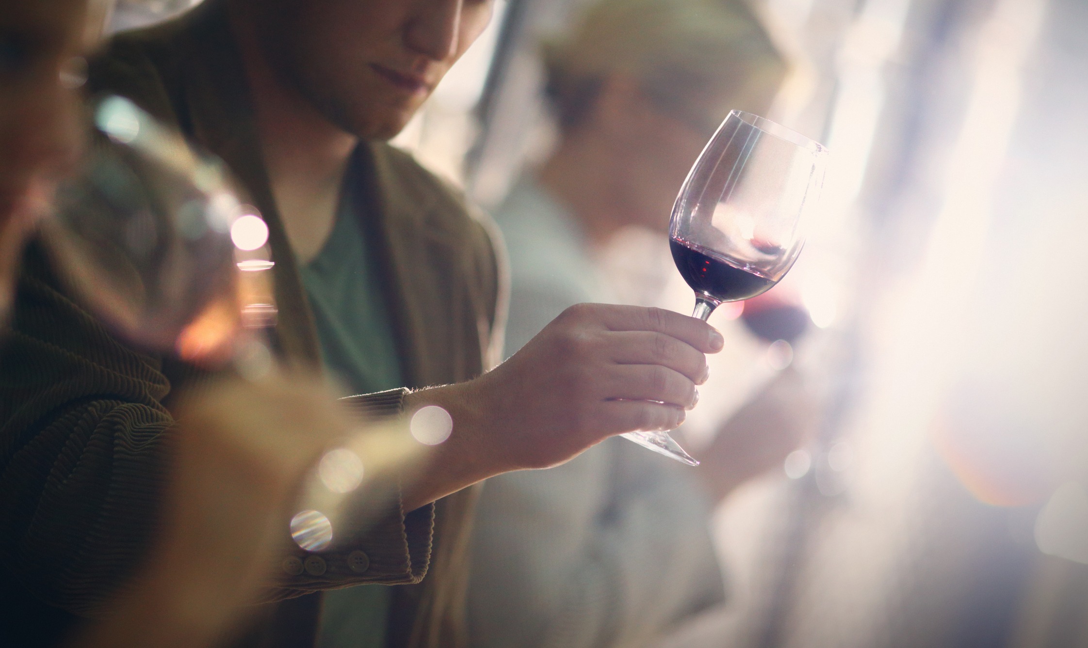 Group of unrecognizable caucasian adults tasting wine in wine cellar. Comparing appearance, smell, aroma,taste,aftertaste. The man in focus is holding a glass of red wine and looking at its color.