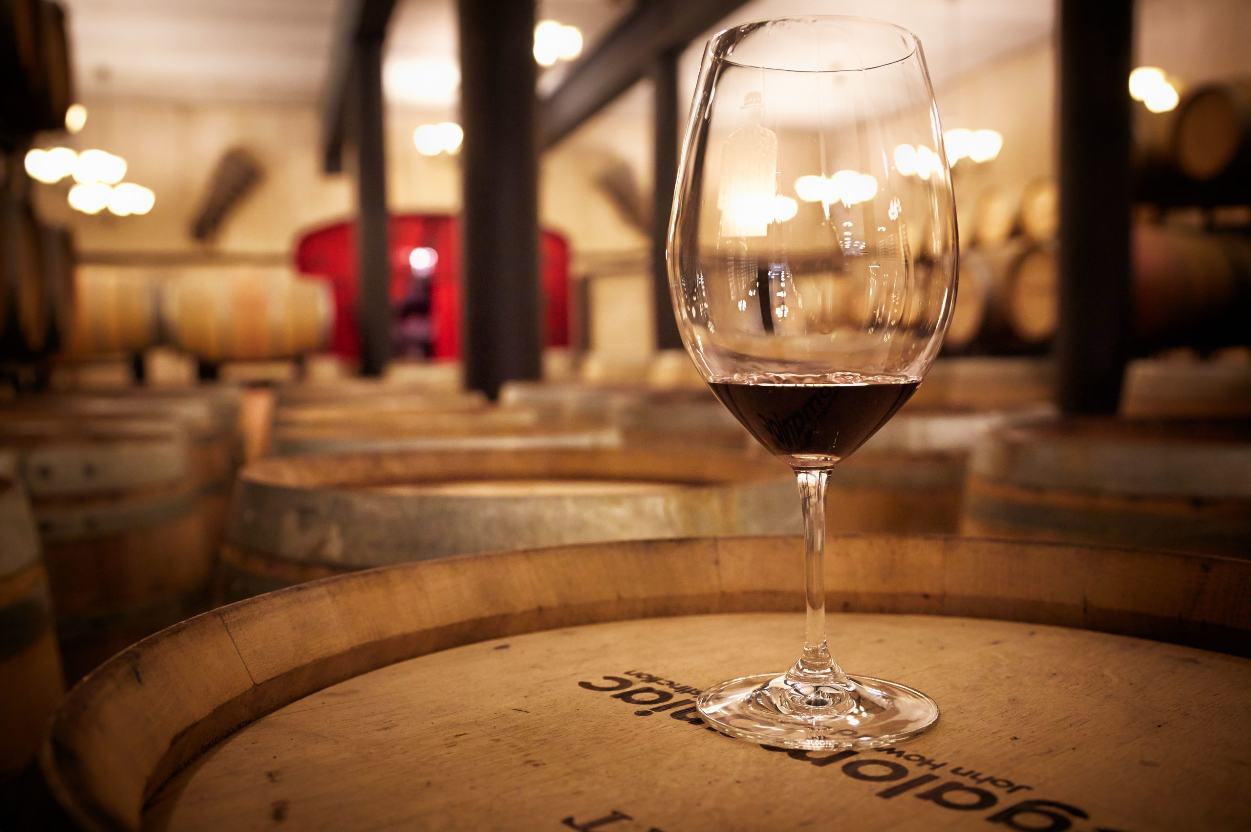 Wine glass on top of a wine barrel in a room filled with wine barrels