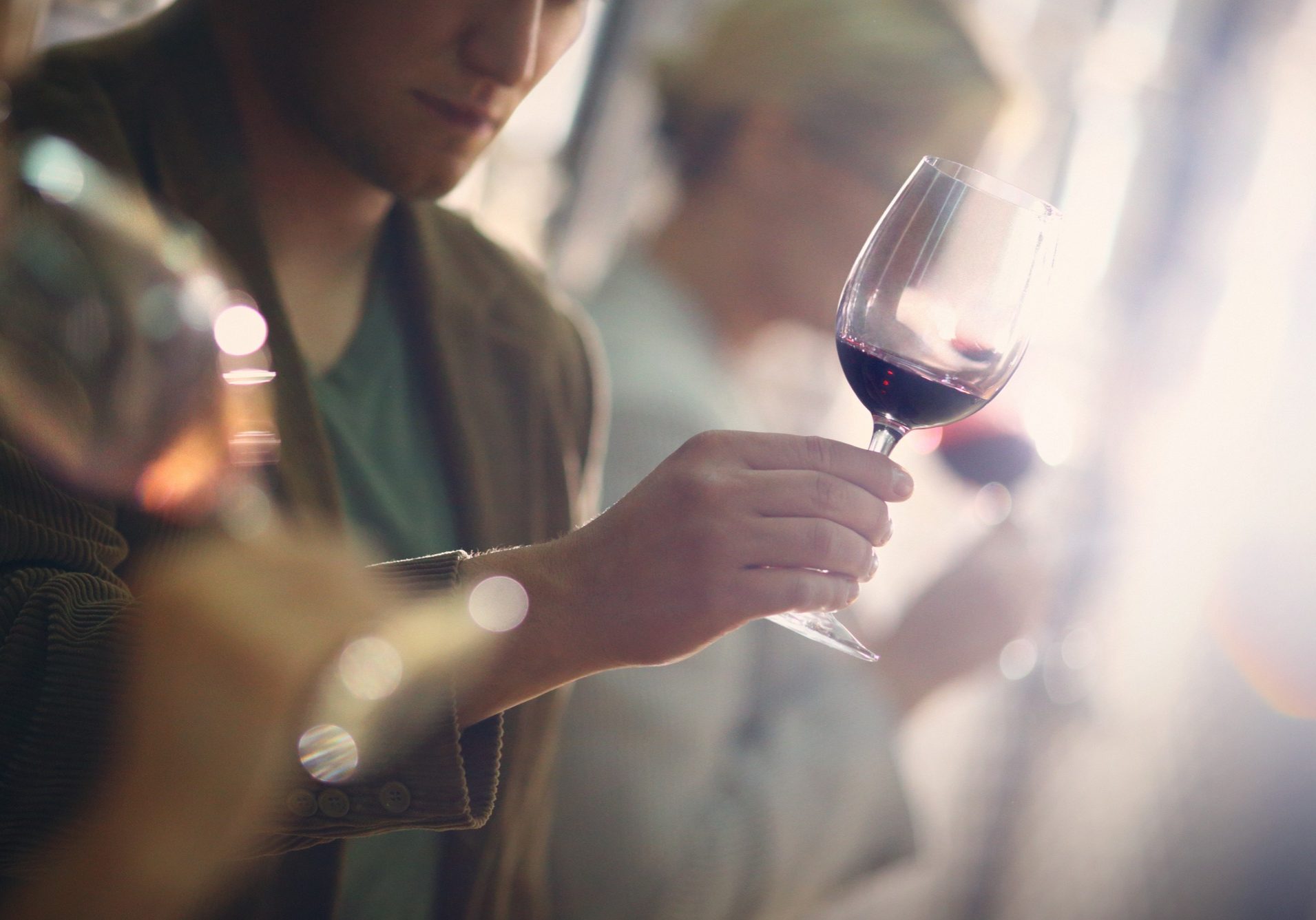 Group of unrecognizable caucasian adults tasting wine in wine cellar. Comparing appearance, smell, aroma,taste,aftertaste. The man in focus is holding a glass of red wine and looking at its color.